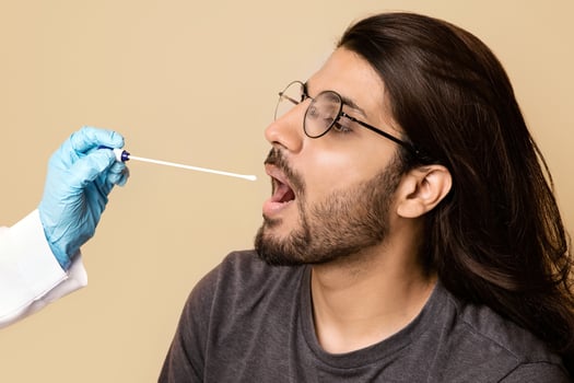 Coronavirus, COVID-19 pcr test concept. Nurse taking oral swab for coronavirus sample test from potentially infected long-haired indian man, beige studio background, closeup, copy space photo