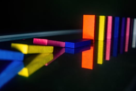 Colorful dominoes in a line, with some fallen over, reflecting on a shiny surface. The vibrant colors and reflections create a visually striking and dynamic composition photo