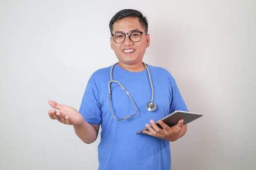 Portrait of happy confident adult asian doctor in white coat, glasses with stethoscope and tablet look at camera isolated on gray background, studio. Medical health care, prescription for treatment photo