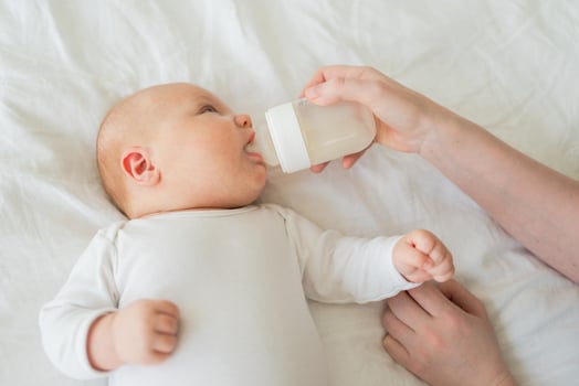 Happy family at home. Mother hand nursing feeding little baby toddler child milk from bottle. Newborn Infant baby girl sucking eating drinking milk. Mom of breast feeding baby. Motherhood happy child photo