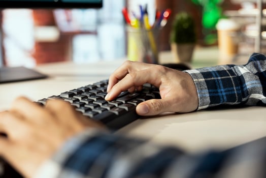 Close up shot of man at home office desk using computer, typing on keyboard, editing documents. Employee at workstation in workspace using PC to complete spreadsheets, solving tasks photo