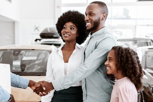 Friendly salesman shaking hands with Afro family, making car purchase agreement at auto dealership. Positive African American clients buying new vehicle, making deal with manager at showroom photo