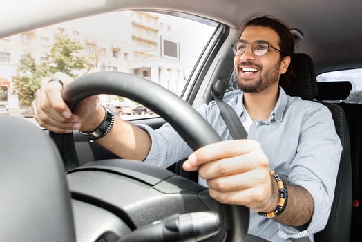 Joyful indian man driving car, shot from dashboard, going on trip during summer vacation, copy space. Happy middle-eastern guy in casual outfit and glasses driving his brand new nice car photo