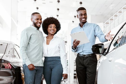 Happy young black couple buying new car together, speaking with friendly salesman at auto dealership. Afro family consulting manager about best luxury vehicle at showroom photo