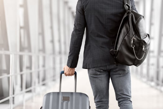 Rear View Of Unrecognizable Male Traveller With Backpack And Suitcase Walking In Airport, Back Shot Of Young Man Passing Terminal Corridor On His Way To Flight Boarding Gate, Copy Space photo