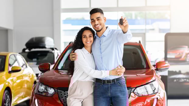 Happy beautiful loving muslim family young arab man and long-haired woman buying new car in salon, standing over red luxury automobile, hugging and showing key from their new auto, copy space photo