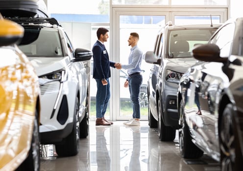 Wealthy middle-eastern man standing among luxury cars in showroom and shaking sales manager hand, celebrating successful deal. Arab guy buying brand new comfortable auto in salon, full length photo
