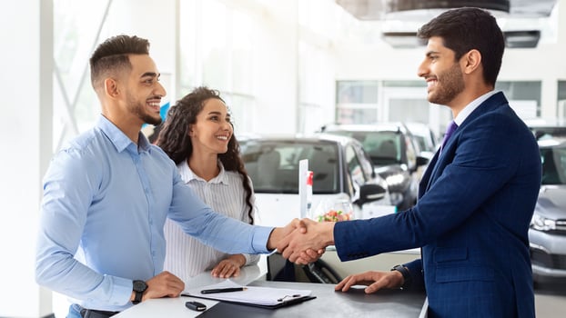 Smiling middle-eastern young man and woman buying car at auto salon, handsome arab guy shaking sales assistant hand, making successful deal, happy family got brand new luxury car, side view photo