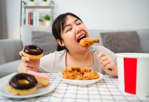 woman is happily eating fried chicken and donuts on a plate. Fast food, Unhealthy food concept. photo