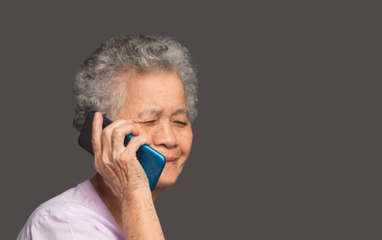 An elderly Asian woman is talking on a smartphone with a smile while standing on a gray background photo