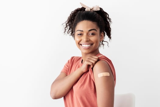 Young african american woman got vaccinated against coronavirus, sitting on chair at clinic, showing medical band on her shoulder, smiling at camera, copy space. Immunization concept photo