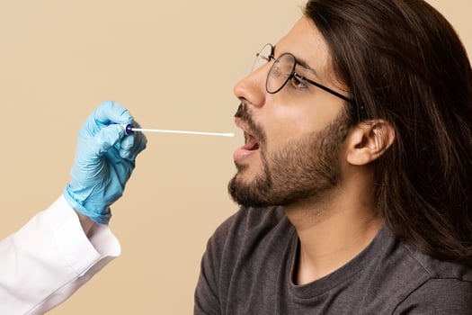 Female doctor in protective face mask making PCR-test for arab guy at clinic, nurse taking oral swab for coronavirus sample, beige studio background. COVID-19 diagnostic, treatment, prevention concept photo