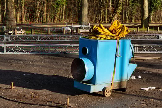 A blue portable air blower sits on a gravel surface, surrounded by photo