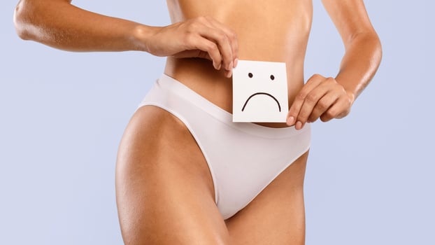 Woman Health Problem. Closeup Of Female With Fit Slim Body In White Panties Holding Paper Card With Sad Smiley Face Near Her Stomach. Digestive Disorders, Period Pain, Health Issues Concept photo