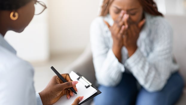 Stressed African American woman consulting psychologist, crying at medical office, selective focus. Psychiatrist helping desperate black lady with nervous breakdown, taking notes during session photo