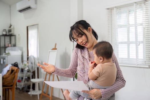 Single mom discussing work on the phone while holding her baby and reviewing important documents at home photo