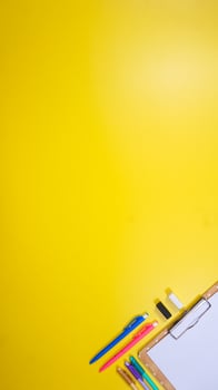 Colorful Pens with Blank Sheet Paper above Wooden Clipboard Isolated on Yellow Background photo