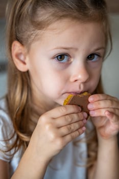 Little girl eating Dubai chocolate with pistachio paste and kataifi dough. Confectionery handmade sweets at home in the kitchen. High quality photo