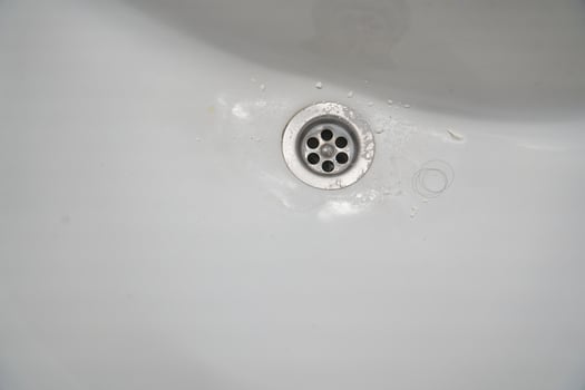 View of a metal drain in a white ceramic bathroom sink. With space to copy photo