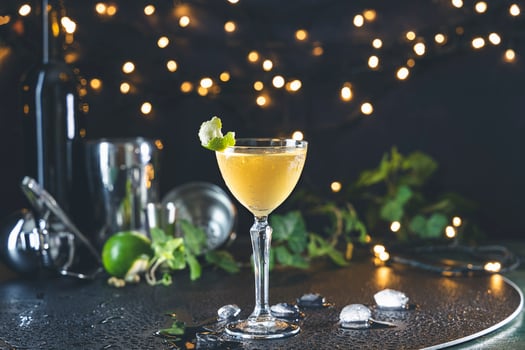 Yellow cocktail garnished with lime and mint on bar top with festive lights photo