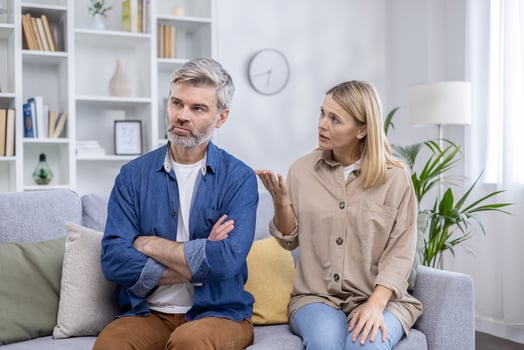A mature man and woman having a serious conversation in a bright, modern living room. The man is upset, folding his arms, while the woman seems to be explaining something. photo