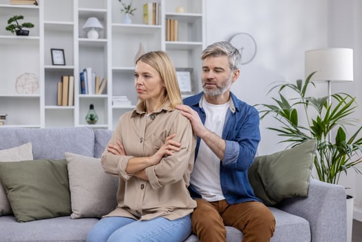 An upset woman and supportive man discussing relationship problems at home. The couple is seated on a couch in a modern living room. photo