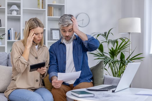 Mature couple looks stressed while managing bills and finances at home, showcasing financial planning challenges in a modern living room setting. photo