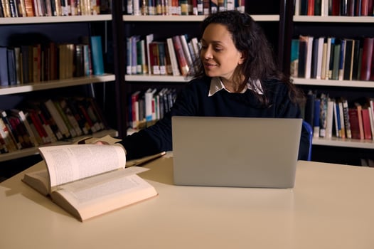 Young woman studying in a library with a laptop and a book photo