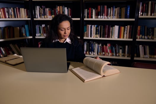 Woman Studying in a Library with a Laptop and Open Book photo