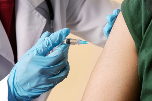Woman doctor making intramuscualr injection against coronavirus for arab guy at clinic, wearing protective face masks, closeup, nurse with syringe vaccinating indian young man while COVID-19 pandemic photo