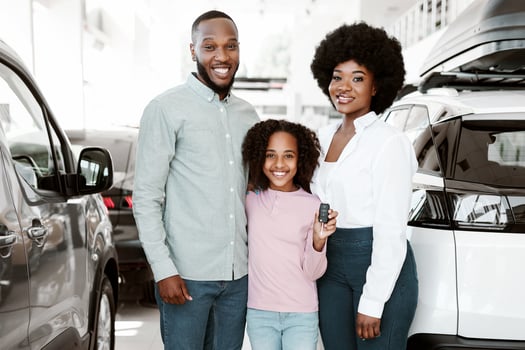 Full length of happy black family holding key, purchasing new car in auto dealership. Young parents with daughter buying vehicle, posing and smiling at automobile showroom photo