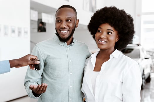 Joyful black couple purchasing new auto, taking car key from salesman at automobile dealership. Happy African American family buying or renting new vehicle at showroom shop photo