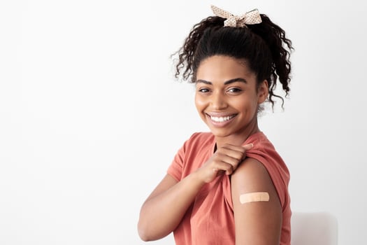 Pretty young black woman showing medical band on her shoulder, cheerful african american lady patient got vaccinated against coronavirus at vaccination center, panorama with copy space photo