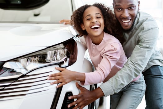 Happy black father and his cute daughter selecting new car, buying or renting automobile at auto dealership. Cheerful Afro family choosing vehicle together at automotive showroom photo