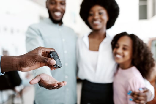 Manager giving new car key to young black family at auto dealership store, selective focus. Happy African American customers buying vehicle from salesman at automobile showroom photo
