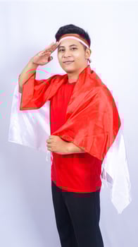 Young Indonesian Man Giving Salute and Holding Indonesia Flag Behind Back photo