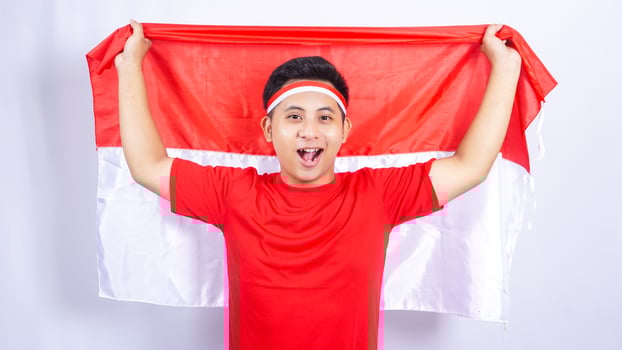 Excited Young Indonesian Man Holding Wide Open Indonesia Flag Behind Back photo