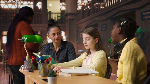 Female tutor mentoring schoolgirls in a school library setting, boosting their understanding of a subject through personalized guidance. Teacher doing private lessons with two pupils. Camera A. photo