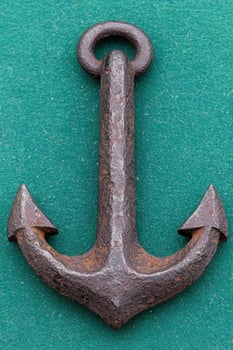 Antique rusty metal anchor on green background photo
