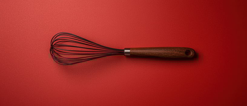 Wooden handled whisk on red background photo