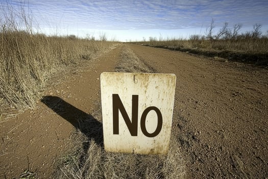 A weathered sign reading No stands on a desolate dirt road photo
