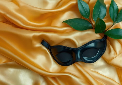 Black masquerade eye mask on gold silk fabric with green leaves photo