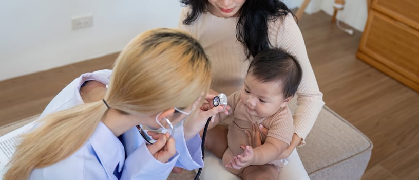 Pediatrician checking baby's heartbeat while mother observes in clinic. photo