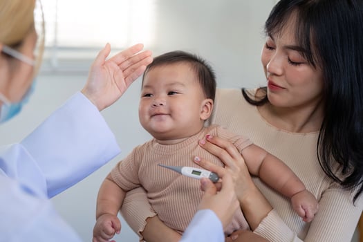 Smiling baby having temperature checked by pediatrician in clinic. photo