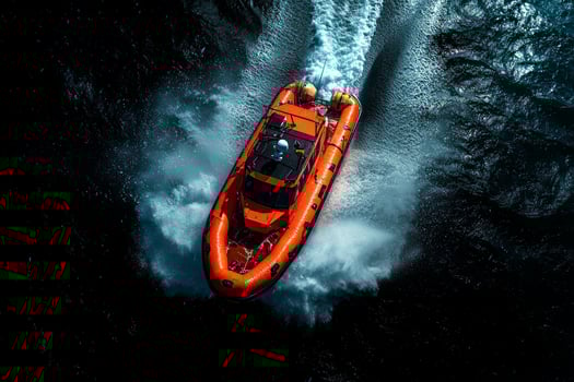 small lifeboat makes its way through relentless waves larger ship faintly visible in background stormy sky. drone captures dramatic conflict of nature photo