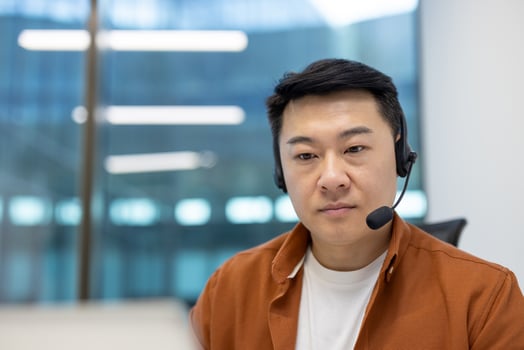Asian man businessman wearing headset engaged in virtual meeting. Office environment, focus on laptop screen, slight smile while listening. Represents communication, technology, productivity. photo