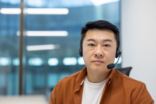 Asian man businessman with headset in office focused on digital communication. Shows modern work environment, casual attire, professional engagement. Represents tech-savvy business practices. photo