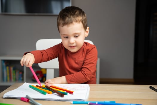 A cute happy little toddler boy of two years old draws with markers in the album in the children's room at home. Educational activities for kids. Selective focus photo