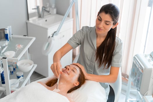 Massage therapist applying face mask to woman with brush at salon photo
