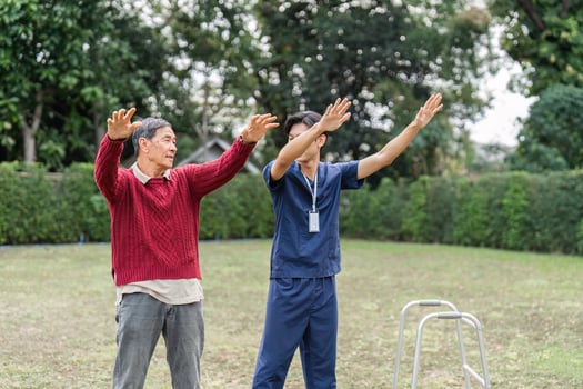 Health caregiver guiding elderly man through physical exercise in the park for rehabilitation photo